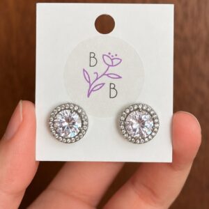 Par de Aretes Allina redondos en tono plateado con brillante central y halo de pequeños brillantes.