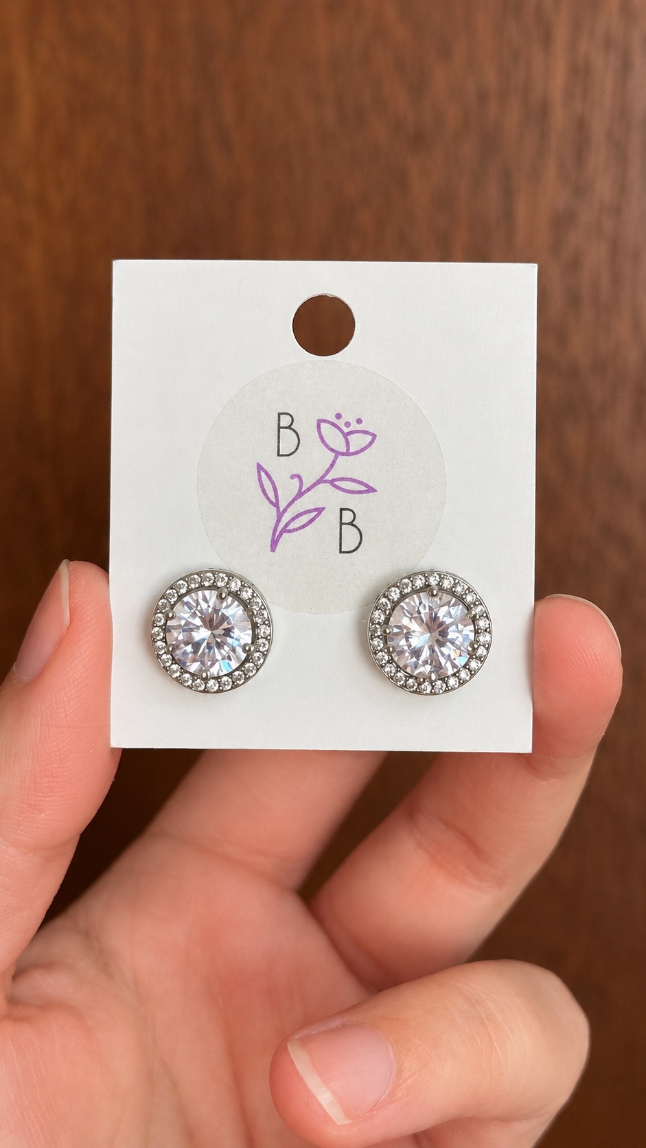Par de Aretes Allina redondos en tono plateado con brillante central y halo de pequeños brillantes.