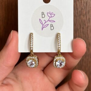 Par de Aretes Lucienne colgantes en aleación de tono dorado con brillantes transparentes.