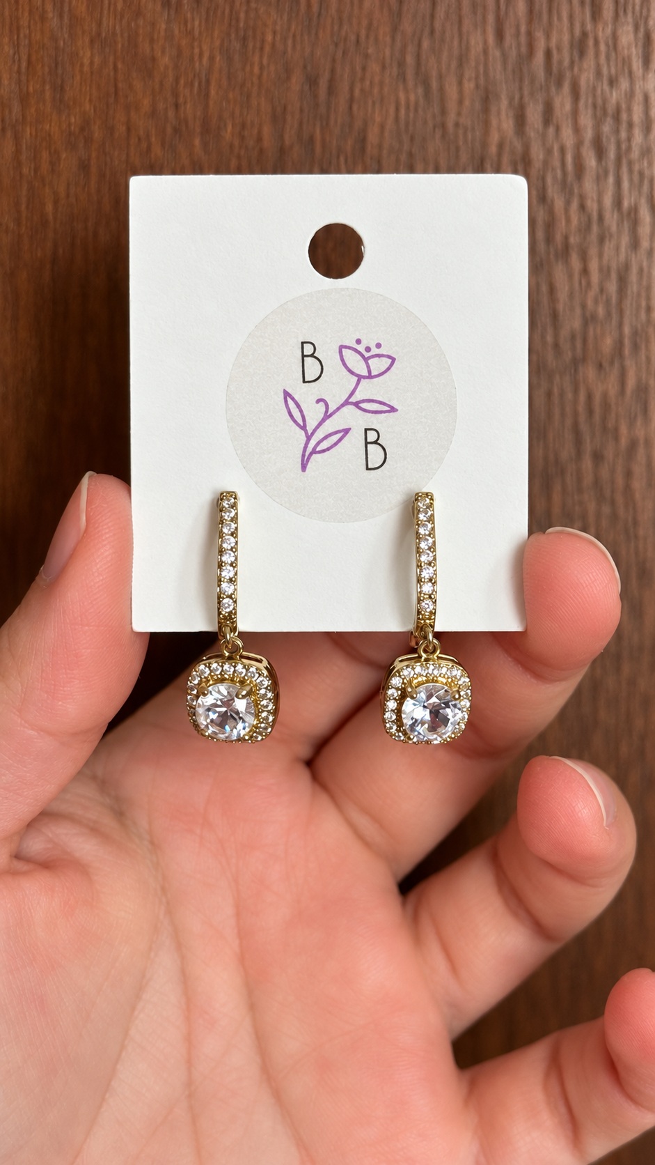 Par de Aretes Lucienne colgantes en aleación de tono dorado con brillantes transparentes.